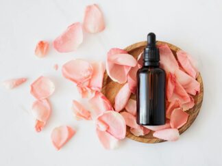 Top view of empty brown bottle for skin care product placed on wooden plate with fresh pink rose petals on white background isolated