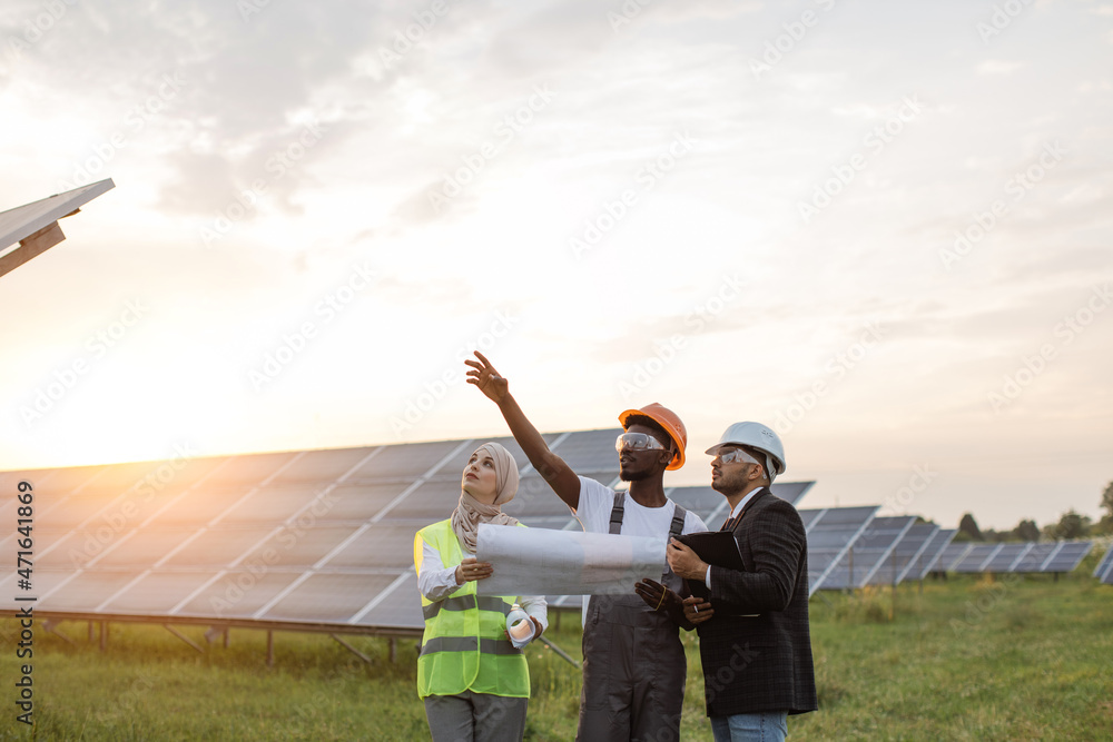 African american technician talking with muslim woman and indian man during working session on solar station. Industrial workers discussing common project of green energy production. Green Business Strategies